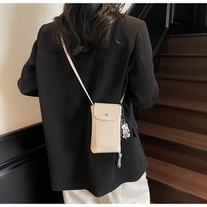Détail du sac de téléphone beige texturé avec charm décoratif et fermeture à pression métal