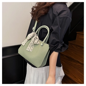 Détail d'un sac cabas vert tressé avec un foulard en soie à pois attaché à l'anse