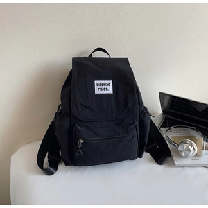 Detail of black nylon backpack featuring a drawstring flap and front zipper pocket