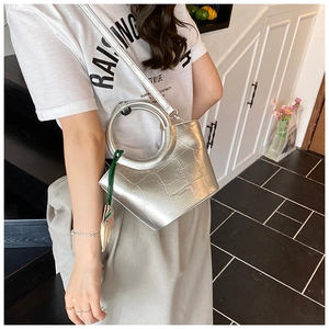 Detail of silver crocodile-embossed bucket bag with unique round handle and green charm
