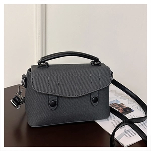 Detail view of structured grey twill handbag with black leather handles on wood surface