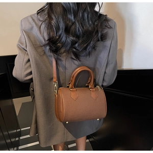 Detail of a brown cylindrical Boston bag showing the smooth leather handle and metal studs