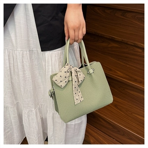 Détail du sac à main en cuir vert clair avec foulard à pois décoratif sur la poignée