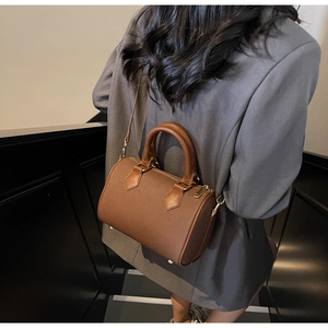 Close-up of a brown leather cylinder Boston bag with gold hardware and shoulder strap