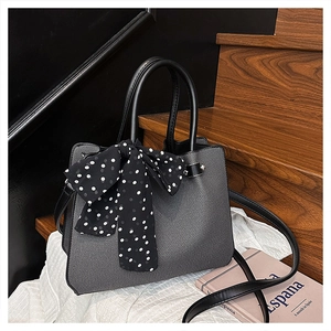Détail du sac seau gris texturé avec foulard à pois et poignée noire sur tissu blanc