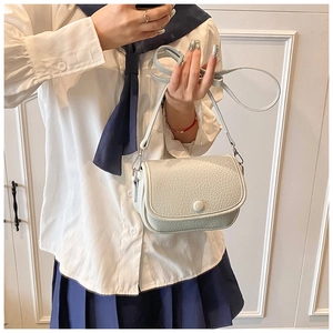 Litchi texture crossbody bag with adjustable strap worn on shoulder against white wall