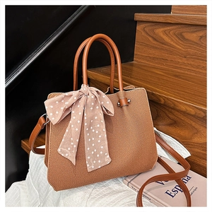 Détail d'un sac cabas marron tissé avec un foulard décoratif à pois sur la poignée