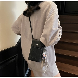 Détail du sac à téléphone en cuir noir avec boucle argentée et breloque ours mignon