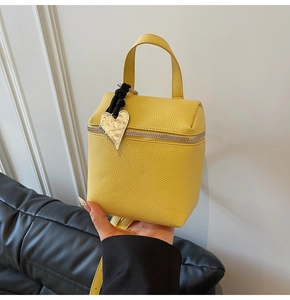 Dettaglio di una mini borsa gialla in pelle a grana con ciondolo a cuore in argento