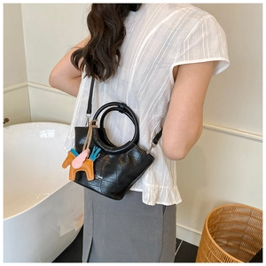 Detail of black crocodile embossed handbag with round handle and orange pony charm