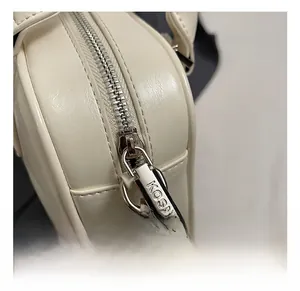 Detail showing the silver metal zipper with KOSK engraving on a creamy white leather bag