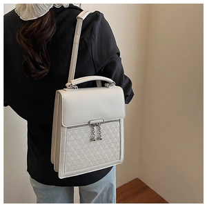 Detail of quilted diamond pattern and metallic chain charms on a beige handbag