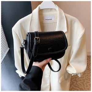 Detail of black textured leather crossbody bag showing flap closure and silver buckle