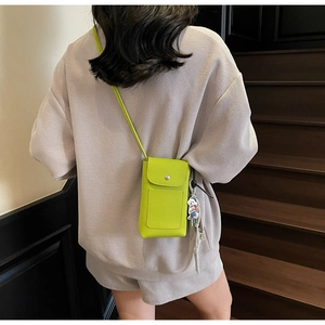 Détail d'une pochette téléphone vert néon en similicuir avec un porte-clé ours mignon