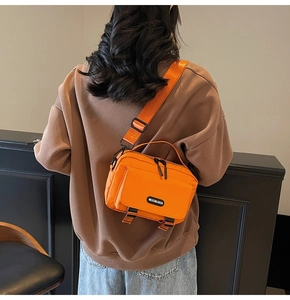 Detailed back view of an orange nylon crossbody bag with black buckle straps and logo