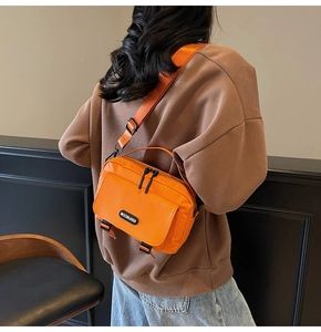 Detail of a bright orange nylon crossbody bag with adjustable strap and buckle on model