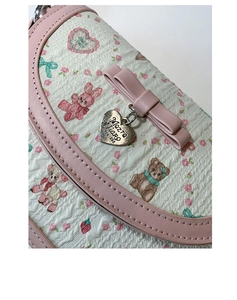 Detail of pink bow and heart pendant on printed crossbody bag with cute animal patterns