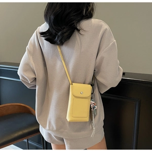 Détail du sac de téléphone bandoulière en cuir litchi jaune avec fermoir à pression et breloque