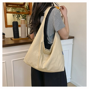 Detail view of large beige canvas tote bag with wide shoulder strap worn in a cafe