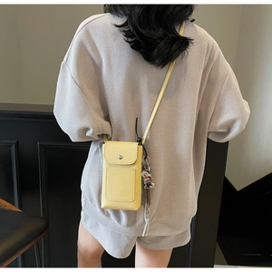 Détail d'un sac téléphone en cuir jaune avec pendentif ours porté par un mannequin