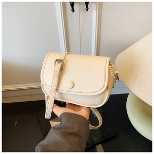 Detail of beige pebble leather crossbody bag with adjustable strap and round metal buckle