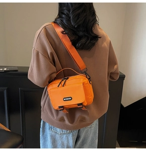 Rear view of model wearing a bright orange nylon crossbody bag with black buckles