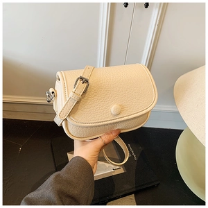 Detailed macro of cream saddle bag featuring lychee texture leather and adjustable strap