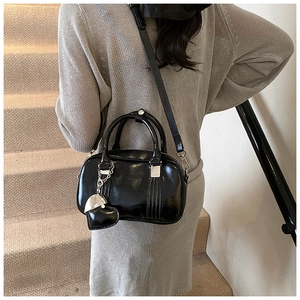 Polished black Boston bag with heart charm and strap worn by model in minimalist setting