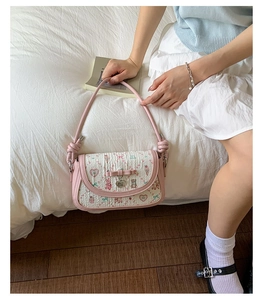 Detail of pink bow and heart pendant on printed crossbody bag with floral patterns