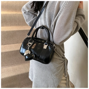 Detail of black glossy PU leather handbag with heart pendant and silver hardware strap