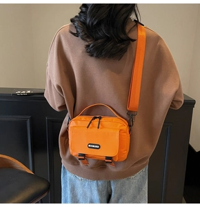 Rear view of model wearing a large orange messenger bag with black buckle closures