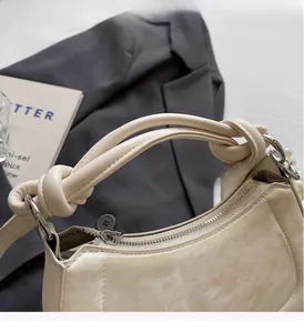 Detail of a creamy white leather handbag featuring a knot handle and pearl charm chain