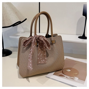 Détail d'un sac cabas tissé beige avec un nœud en foulard à pois et des anses en cuir