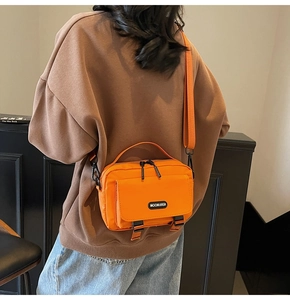 Rear view of model wearing a large orange nylon crossbody bag with buckle and brand logo