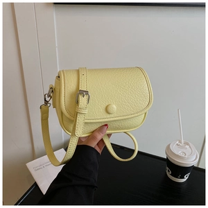 Detail showing cream leather crossbody bag with lychee texture and round buckle