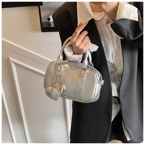 Detail of silver metallic handbag with heart charm and glossy finish in studio setting