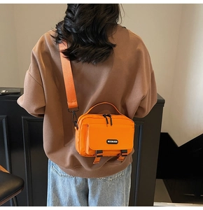 Detail of a bright orange crossbody bag featuring a front pocket with black buckle closure