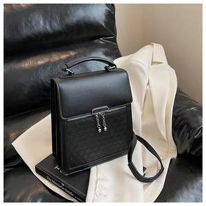 Close-up of black leather handbag featuring geometric embossed patterns and chain pendant
