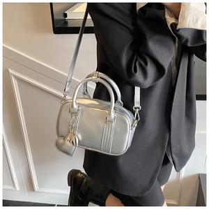 Detail of silver metallic Boston bag with heart charm and crossbody strap on a model