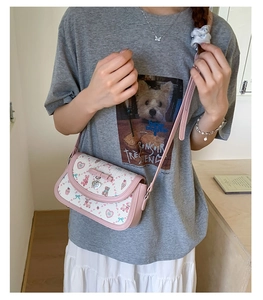 Detailed view of pink shoulder bag with bear prints and heart charm worn by a model