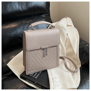 Detail of beige quilted handbag with metal ball zipper pull on leather sofa