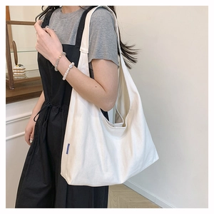 Detail of white canvas tote bag featuring wide strap and blue side brand tag label