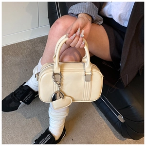 Detail view of cream handbag with heart charm and twin handles in a street style setting