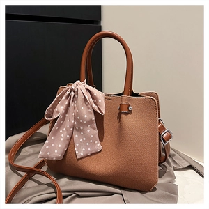 Détail d'un sac seau marron avec un foulard à pois rose et une bandoulière réglable