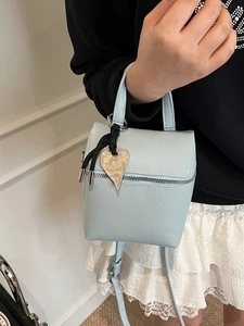 Mini borsa a mano azzurra con trama litchi e ciondolo a cuore dorato su modella