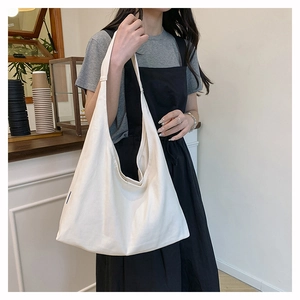 Spacious off-white canvas tote bag shown on a model in a minimalist cafe setting