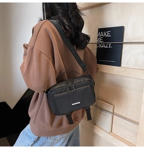 Rear view of model wearing black nylon crossbody messenger bag with buckle detail