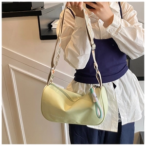 Détail du sac bandoulière cylindrique vert clair avec sangle tissée et breloque nouée
