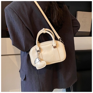 Detail of creamy white crossbody bowling bag featuring a heart pendant and KOGSK logo