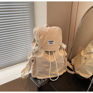 Detail of a cream nylon backpack with flap buckle closure and drawstring on a desk
